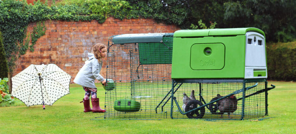 girl feeding her hens in a green eglu cube chicken coop
