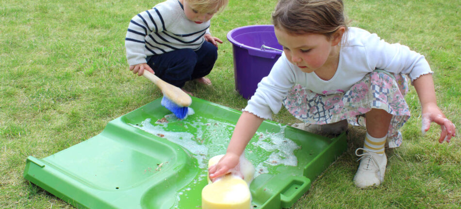 Kinderen maken een onderdeel van een Omlet Eglu Cube kippenhok schoon