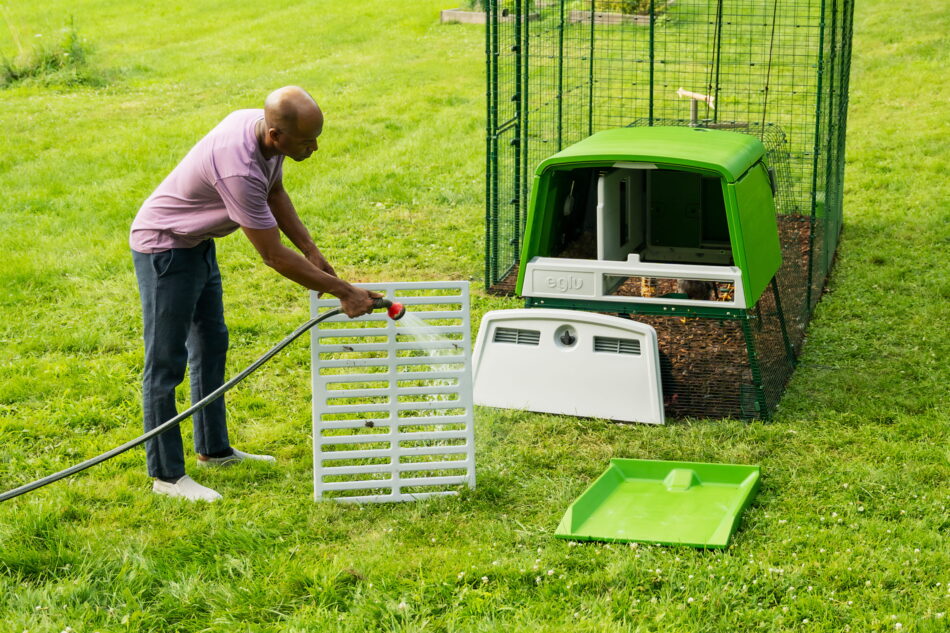 man cleaning roosting rack with a hose