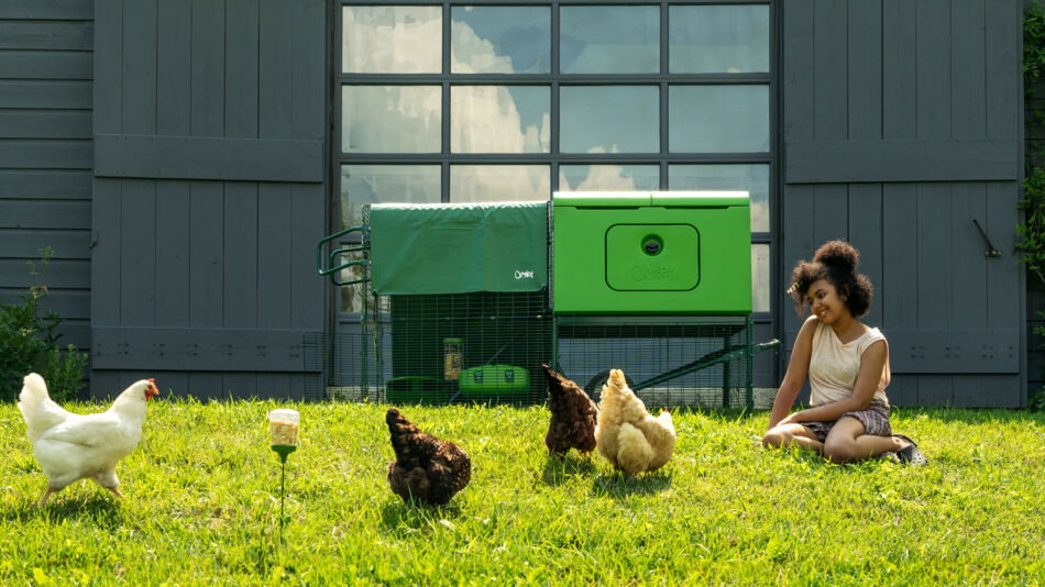 Girl sat in the yard with fee ranging chickens by Omlet Eglu Cube