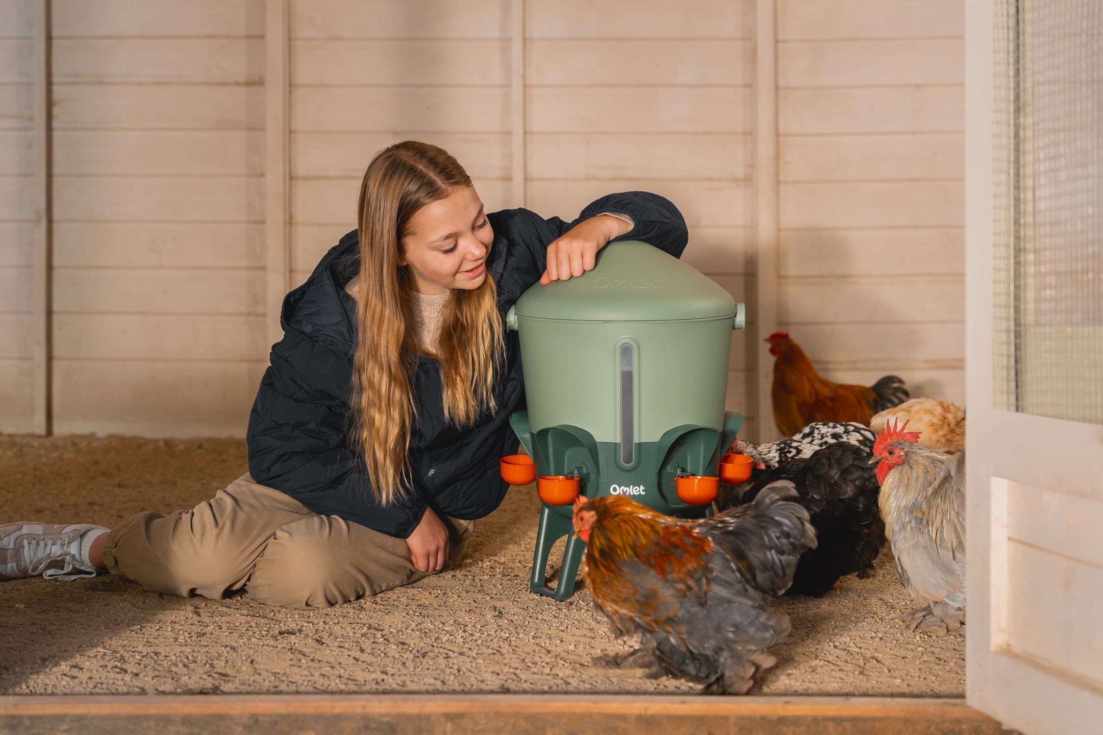 girl sitting next to water drinker with chickens drinking from cups