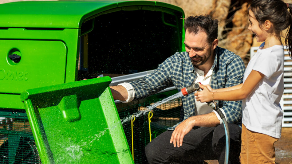 Man and girl cleaning the Omlet Eglu Pro roosting tray with hose