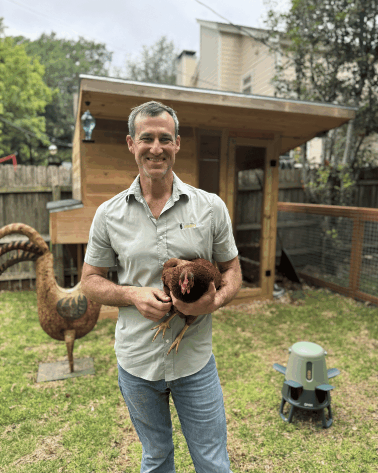 Dr Blayne in his garden, holding a chicken, Omlet Smart Feeder in the background